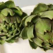 Two fresh green artichokes on a white plate