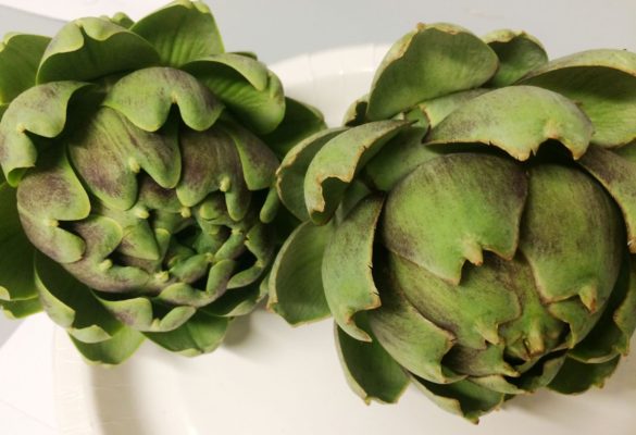 Two fresh green artichokes on a white plate