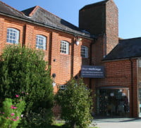 Red brick building with gardens in front and a glass porch