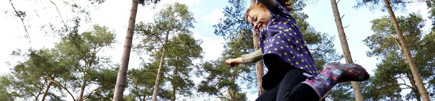 Girl leaping in the air. Tall trees in background