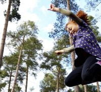 Girl leaping in the air. Tall trees in background