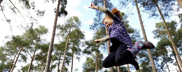 Girl leaping in the air. Tall trees in background