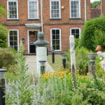 Back of red brick building, male bust in background, flowers in foreground.