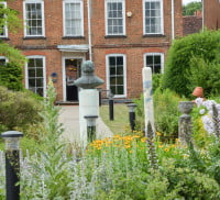 Back of red brick building, male bust in background, flowers in foreground.