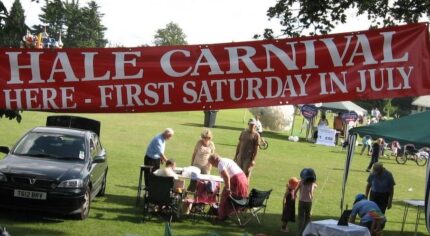 Banner advertising Hale Carnival. People setting up stalls for fete.