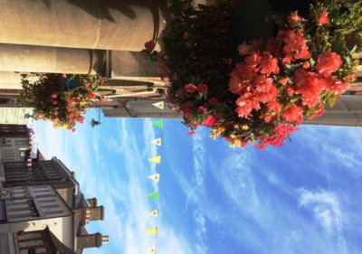 Hanging baskets on side of building. Street scene with blue sky.