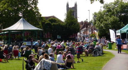 Crowd of people in park, with bandstand and gazebos.