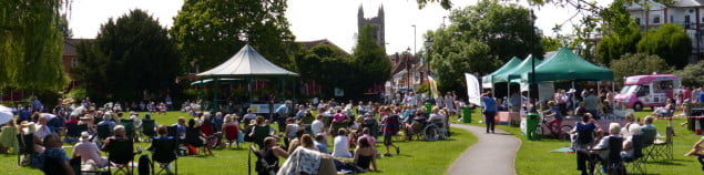 Crowd of people in park, with bandstand and gazebos.