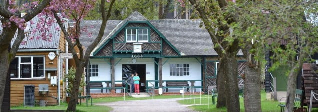 exterior of white wooden buiding, with green pillars. Trees and pathway in foreground.