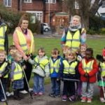 Group of boys, girls and four women with high vis vests in park.