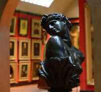 Bust of female head and shoulders on a plinth. Art gallery in the background