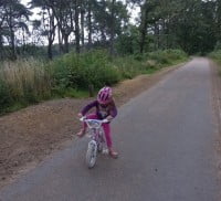 child on bike, woodland surrounding pathway.