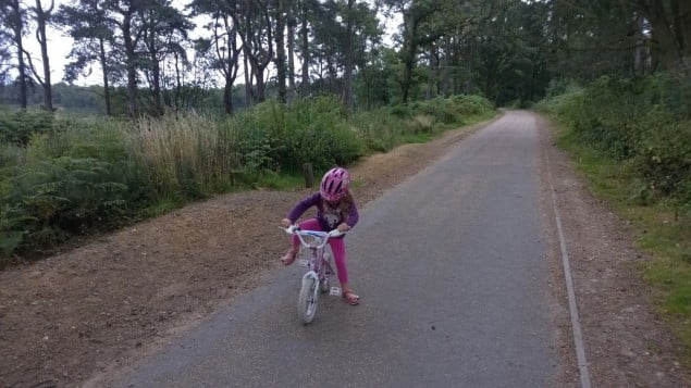 child on bike, woodland surrounding pathway.