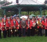 Group of male and female brass band members standing in front of band stand.