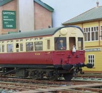 Red and cream train on a railway track, yellow building to the right, red and green building on the left.