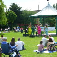 People watching three female singers at Music in the Meadow. © Farnham Town Council