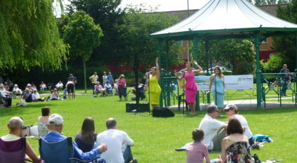 People watching three female singers at Music in the Meadow. © Farnham Town Council
