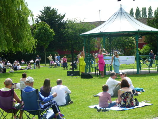 People watching three female singers at Music in the Meadow. © Farnham Town Council