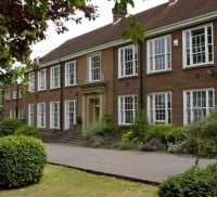 Exterior of wide red brick building with tiled roof and multiple white-framed windows. Path and grass in front.