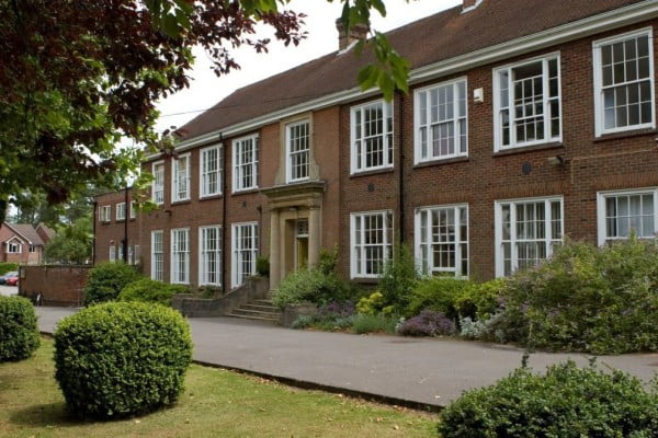 Exterior of wide red brick building with tiled roof and multiple white-framed windows. Path and grass in front.