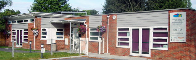 Outside Hale Community Centre. Red brick bungalow. Trees in background and grass in front