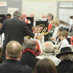 group of children playing instruments, smartly dressed. Audience in foreground.