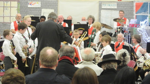 group of children playing instruments, smartly dressed. Audience in foreground.