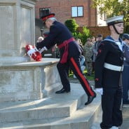 Male laying wreath on war memorial, group to the right watching, male in uniform in foreground