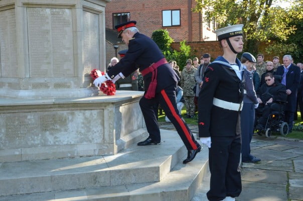 Male laying wreath on war memorial, group to the right watching, male in uniform in foreground