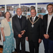 Six people standing in a row in front of an exhibition.