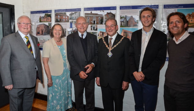 Six people standing in a row in front of an exhibition.