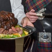 Chef holding venison joint on silver tray and piper holding bag pipes.