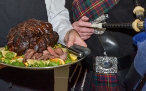 Chef holding venison joint on silver tray and piper holding bag pipes.