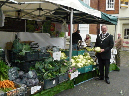 Mayor holds a cauliflower in front of vegetable stall at Food Festival.