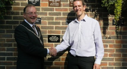 Mayor and man shake hands in front of brick wall after unveiling a commemorative plaque.