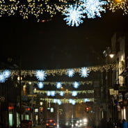 Across street Christmas lights.White stars and gold lights. Busy street. Nighttime.