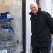 Snowman made from tinsel with blue top hat. shop window. man looking through window at snowman