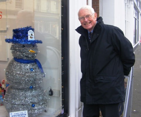 Snowman made from tinsel with blue top hat. shop window. man looking through window at snowman