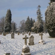 Snow, grave stones, trees in background, blue sky