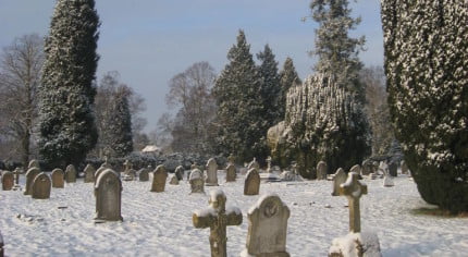 Snow, grave stones, trees in background, blue sky