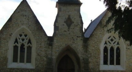 Outside stone chapel, bell turret, arched windows and door.