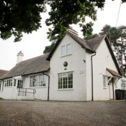 Outside of white-walled village hall with parking in front.
