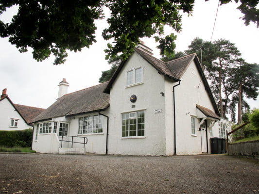 Outside of white-walled village hall with parking in front.