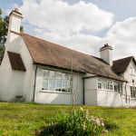 Front of village hall with white walls, tiled roof and chimney on left hand side of building