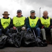 Males in yellow high vis vests with black sacks of rubbish.