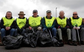 Males in yellow high vis vests with black sacks of rubbish.
