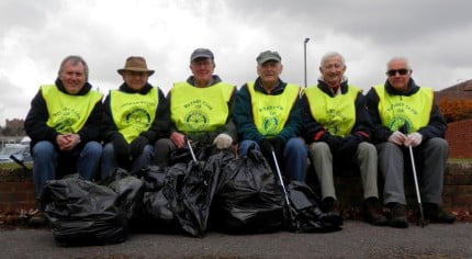 Males in yellow high vis vests with black sacks of rubbish.