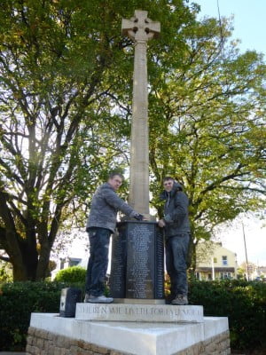 2 males standing on a memorial, trees in background.