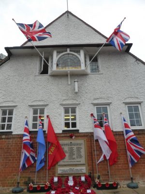 War memorial on wall of building with flags either side and poppy wreaths at base.