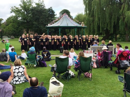 A group of singers performing to a crowd in the park.